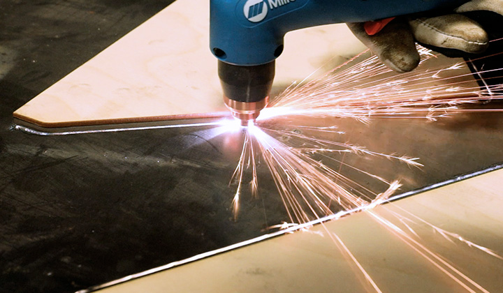 Close-up on operator plasma cutting around a wooden pattern on metal