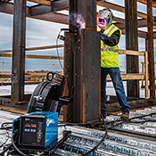 Operator welds on a structural steel jobsite with welding power source in the foreground