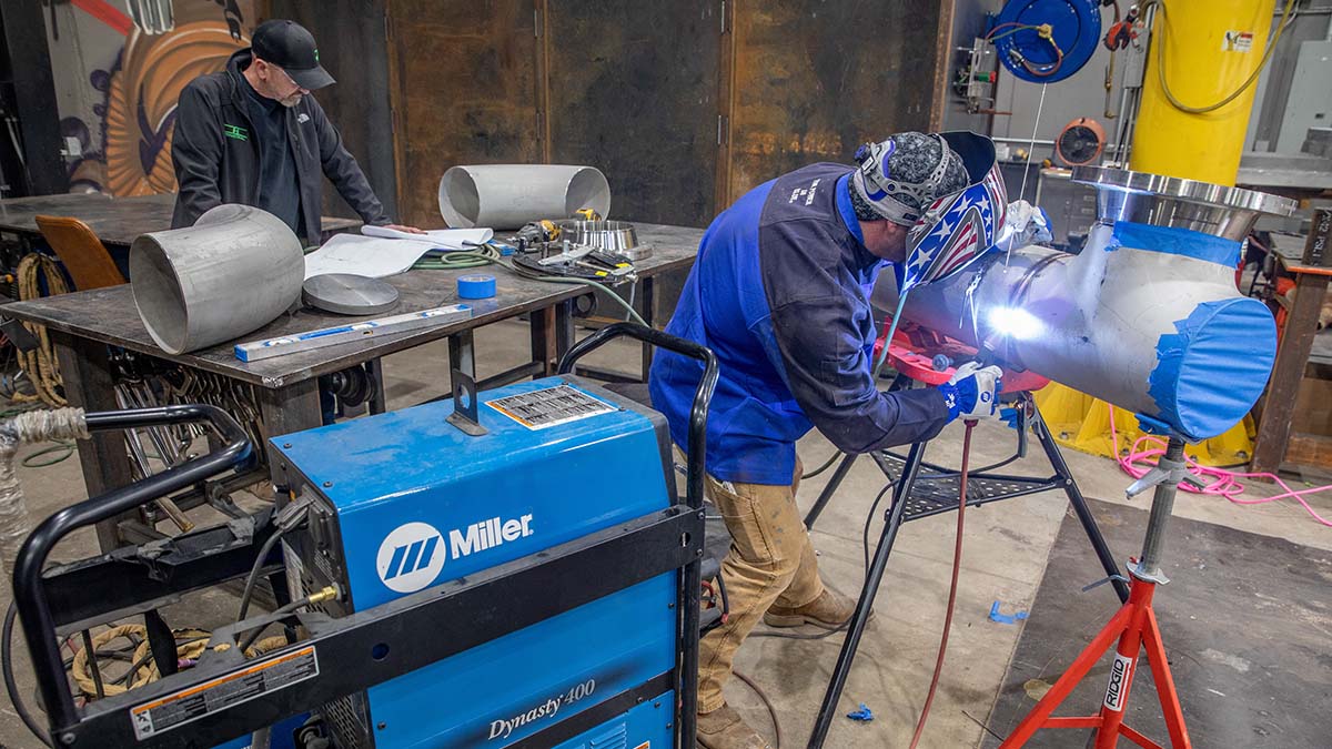 A person inside T&T Industrial TIG welding a metal pipe using a Miller welder.