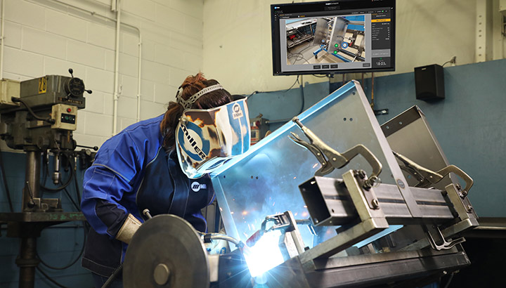 An operator welds while a screen in the background shows real-time guidance