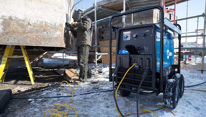 Operator grinds on a jobsite with an engine-driven welder/generator in the foreground