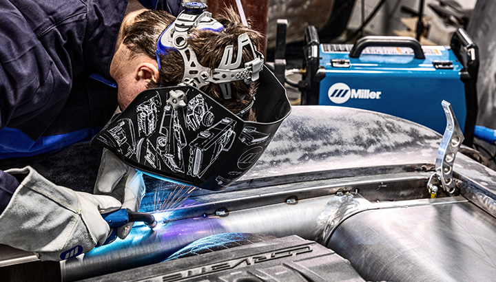 Close up of welder MIG welding on car engine component with welding machine in the background