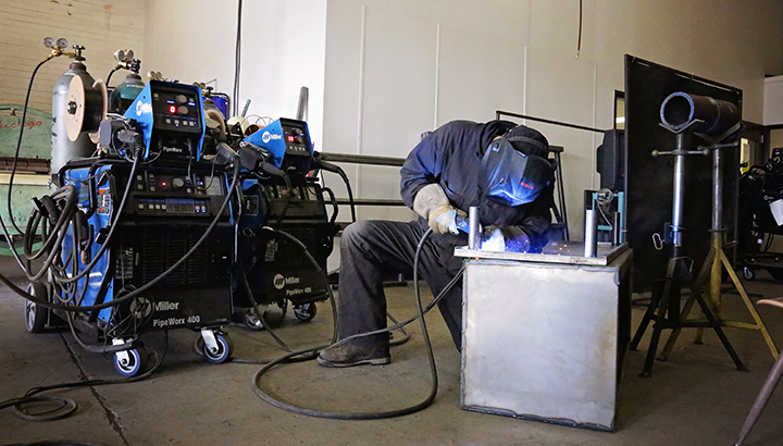 Student welding on a large metal box with welding equipment next to him