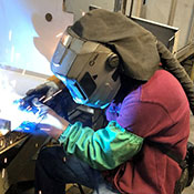 Welding operator welding in the shop wearing Powered Air Purifying Respirator