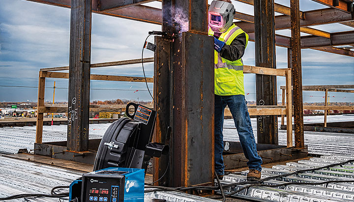 Operator welds on a structural steel jobsite with welding power source in the foreground 