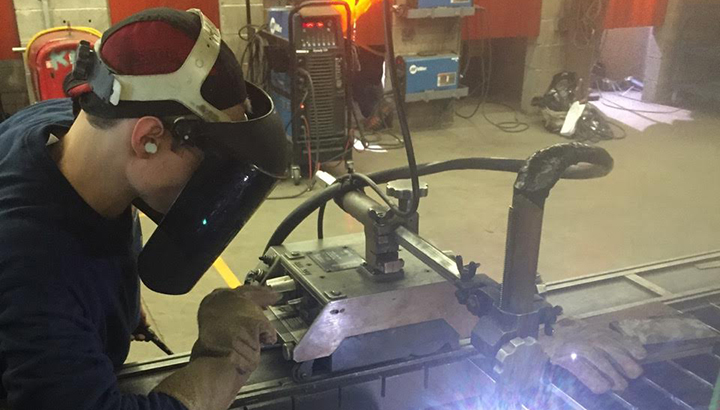 Student wearing helmet, standing near welding machine and arc
