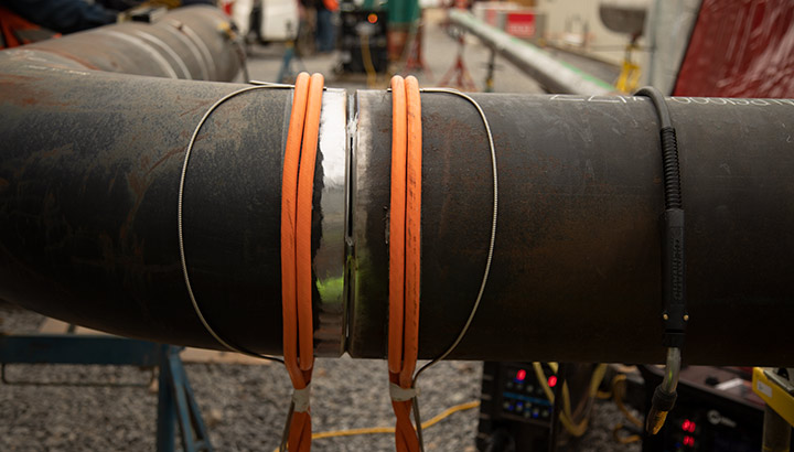 Orange air-cooled cables for induction heating wrapped around a pipe on a jobsite