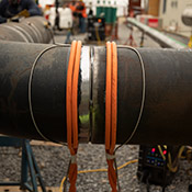 Orange air-cooled cables for induction heating wrapped around a pipe on a jobsite