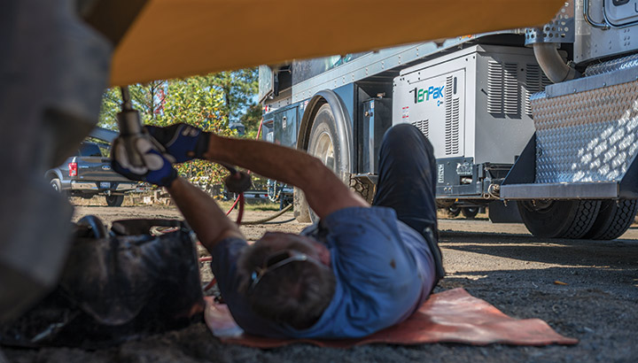 Lube truck mechanic lies under a piece of heavy equipment to service it