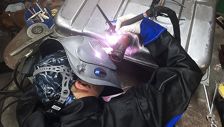 Close up of an operator bent over a piece of metal he is welding