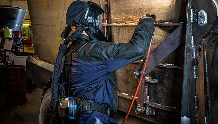 Operator grinds a weld while wearing a Face Shield Powered Air Purifying Respirator (PAPR) from Miller