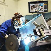 Operator welds on a part with training instructions on a screen behind them