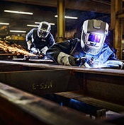 Two operators working on a large flat structure, one welding and one grinding