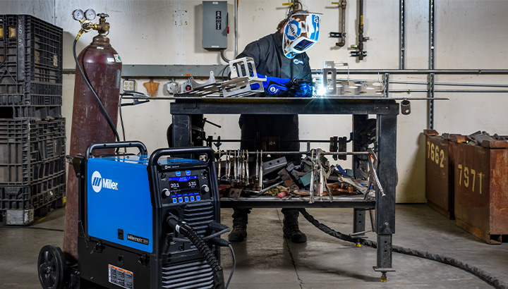 Operator welding aluminum in a shop with Millermatic 355 shown in front of the workbench