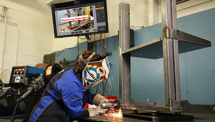 Operator grinds a weld with post-weld instructions on a screen