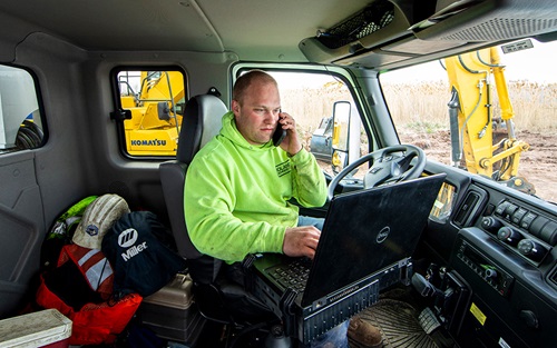 Service technician talks on his cell phone and looks at his laptop inside a service truck on a jobsite