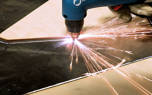 Closeup of operator plasma cutting metal around wood pattern
