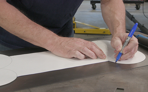 Operator outlining paper pattern onto metal with marker