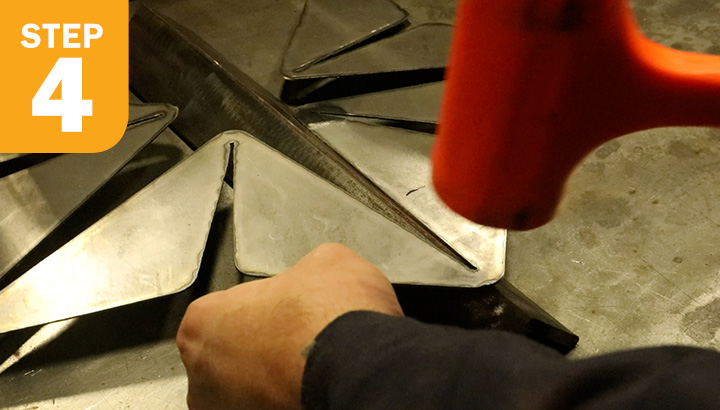 Welder using orange dead blow hammer to pre-crease folds into metal over angle iron