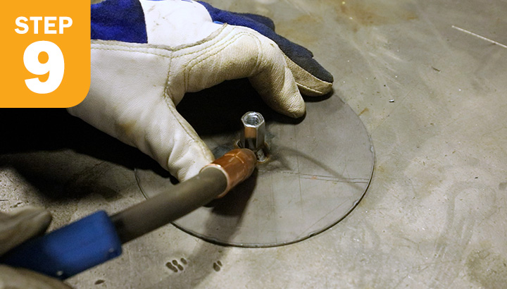 Close-up of operator using MIG gun to tack weld nut to metal disk