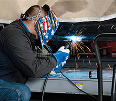 Operator kneels to weld on the bottom of a car on a lift