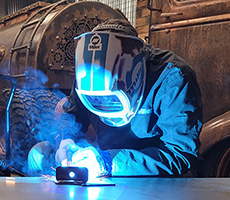 Welder MIG welding at table with MIG welder and gas canister in background